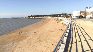 Een strand met een wandelpad, mensen die wandelen, en gebouwen op de achtergrond.