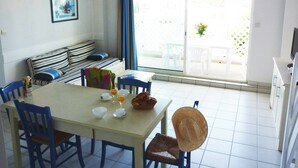 Een eethoek met een tafel voor twee personen, stoelen, een bank met gestreepte kussens, een wandlamp en een raam met uitzicht.