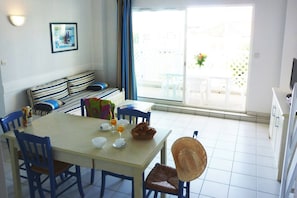 A dining area with a table set for two, chairs, a sofa with striped cushions, a wall-mounted light, and a window with a view of the outside. - Apartment in France with Ocean View (Fouras)
