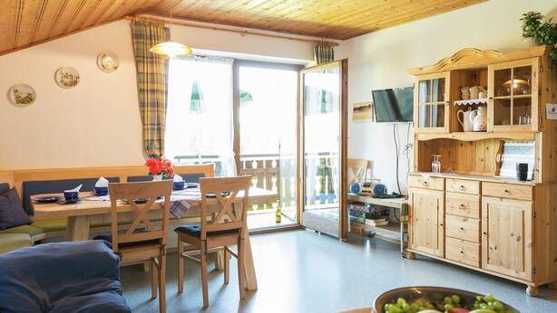 A cozy room with a dining table, chairs, a sofa, a kitchen area with cabinets, and a television. - Alpiner Aufenthalt mit Balkon in Steingaden (Steingaden)