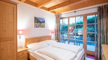 A room with a wooden ceiling, a bed with white bedding, a nightstand, a wall-mounted lamp, and a window with curtains.