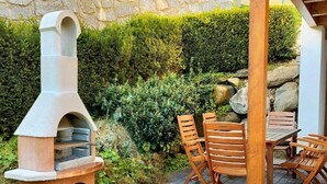 An outdoor patio with a stone-built wood-fired pizza oven, a wooden table, and chairs.