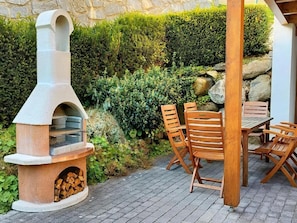 Un patio al aire libre con un horno de pizza de leña de piedra, una mesa de madera y sillas.