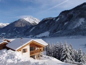 A wooden chalet with a snow-covered roof, surrounded by a snowy landscape and mountains. - Charming Detached Chalet in Wald im Pinzgau (Wald-Königsleiten)