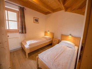 A bedroom with two single beds, a window with curtains, a radiator, and a wooden ceiling. - Charming Detached Chalet in Wald im Pinzgau (Wald-Königsleiten)