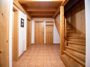 Un pasillo con puertas de madera, suelo de baldosas y una escalera de madera.