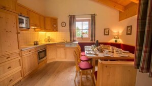 A wooden kitchen with a dining area, a microwave, and a window with curtains.