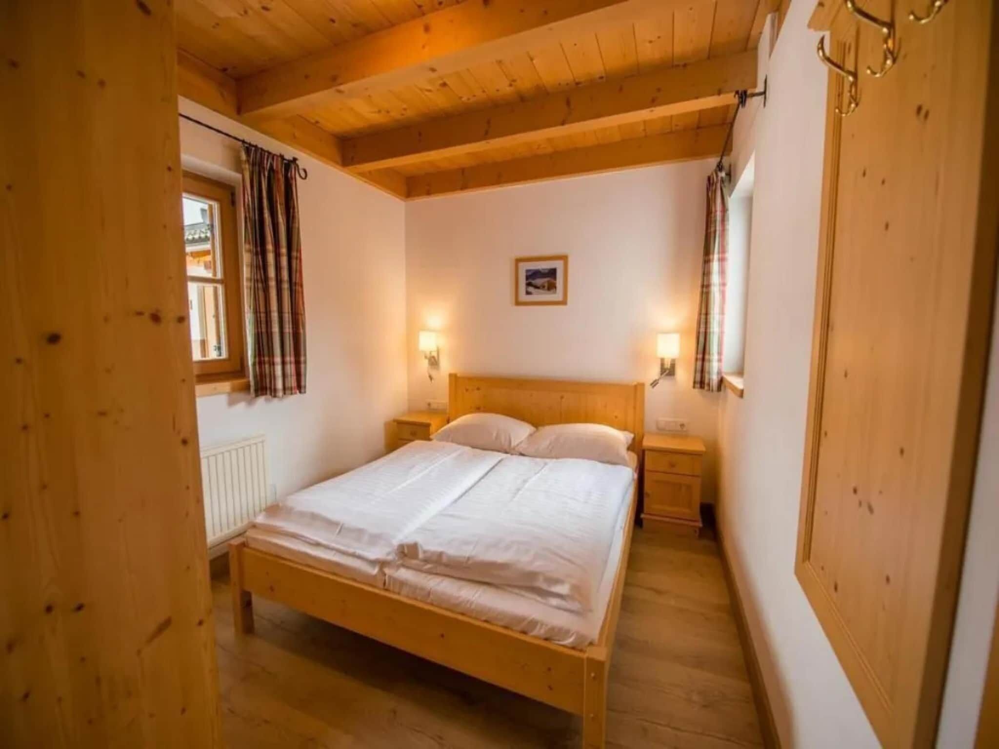 A wooden-framed room with a bed, two bedside tables, and a window with curtains.