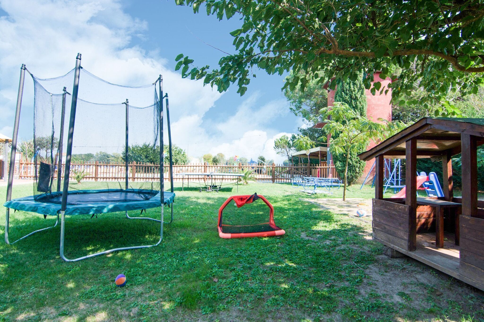 Une aire de jeux avec un trampoline, une balançoire et un toboggan.