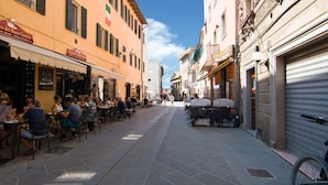 A narrow street with outdoor seating at cafes, a bicycle parked on the right, and buildings with shutters and awnings. - Belvilla by OYO Large Farmhouse with Pool (Castiglione del Lago)