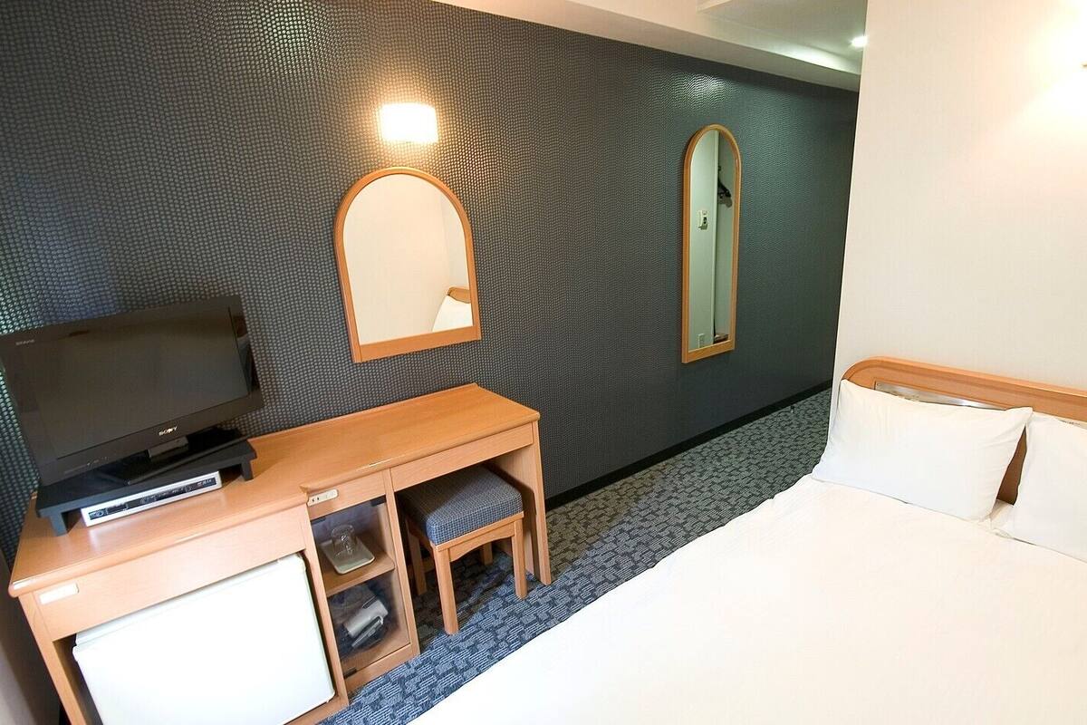 Une chambre d’hôtel équipée d’un lit, d’un bureau avec une télévision, d’un miroir et d’une lampe fixée au mur.