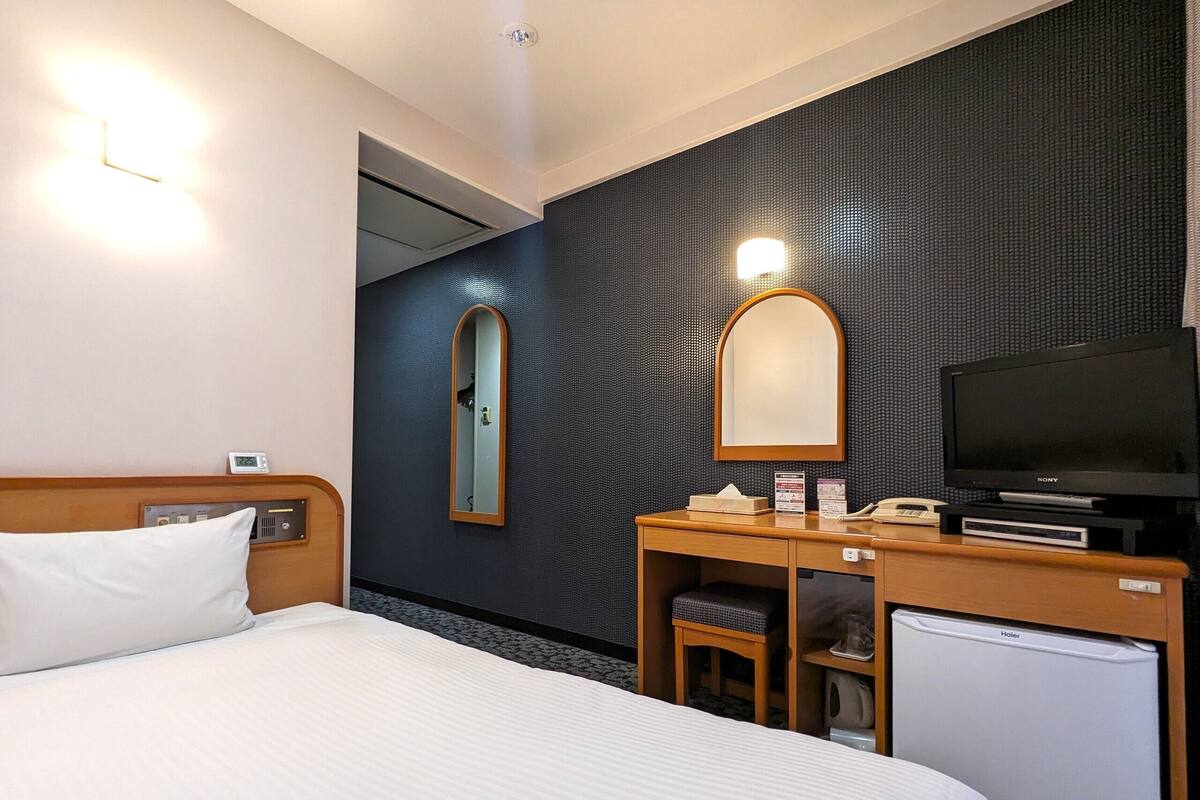 Une chambre d’hôtel comprenant un lit, un bureau avec un miroir, une télévision et un petit réfrigérateur.