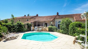 A pool area with a tiled deck, a stone wall, and a building with a tiled roof in the background. - Holiday Home Saint-Laurent Pool & Garden (St. Laurent de la Salle)