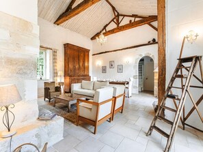 Un intérieur rustique avec des poutres apparentes, un lustre, un ensemble de canapés et une échelle.