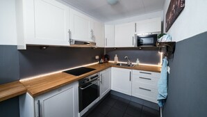 Cozinha moderna com armários brancos, bancada de madeira, forno embutido e micro-ondas.
