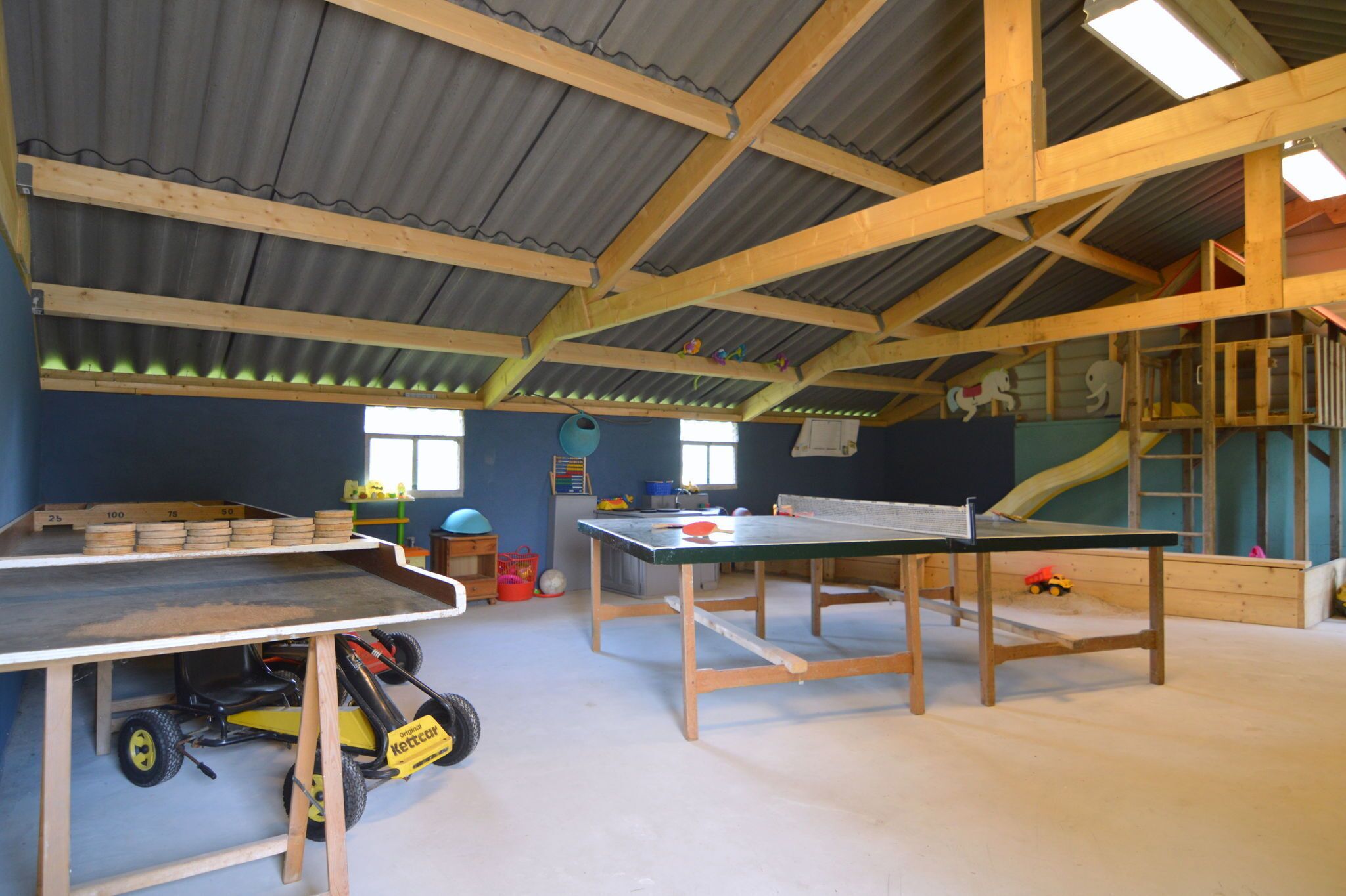 En rummelig stue med højt til loftet, træbjælker og et ping pong bord.