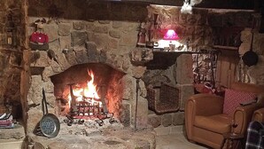 A stone fireplace with a fire, a leather armchair, and a small table with books.