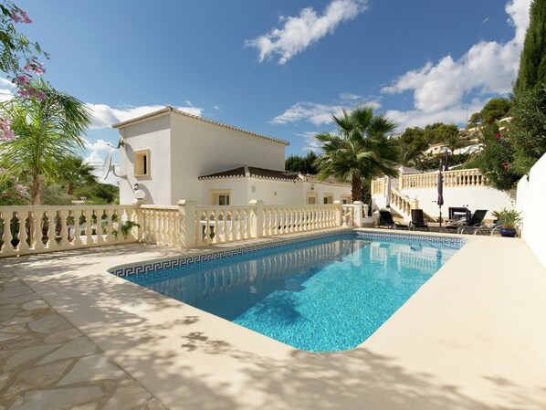 A swimming pool with a white fence, a white building with a balcony, and palm trees.