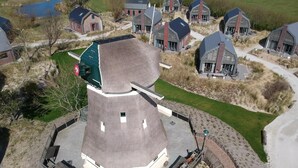 A modern building with a unique conical roof, surrounded by smaller houses with similar architectural styles. - Holiday Home in Egmond near the Beach (Egmond aan zee)