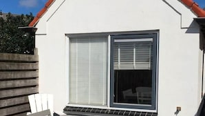 A white building with a red roof, a large window with blinds, and a small porch area. - Holiday Home in Egmond near the Beach (Egmond aan zee)