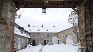 A snow-covered courtyard with stone buildings, a stone pathway, and a hanging lantern.