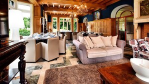 A spacious living room with a high ceiling, wooden beams, and a chandelier. There is a dining area with tables set for a meal. - Luxury Estate with Pool & Spa (Jamoigne)