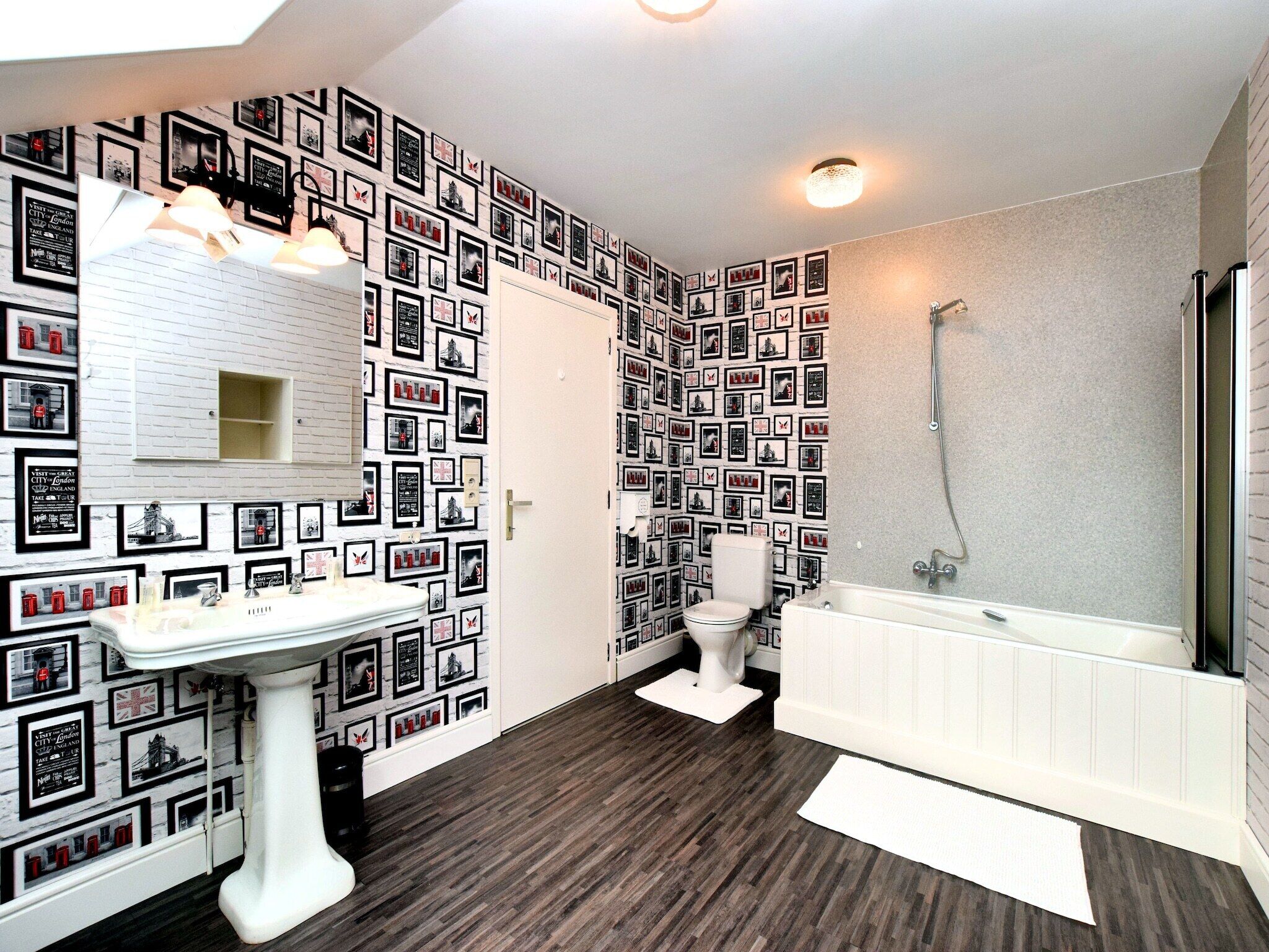 Une salle de bain avec un lavabo sur pied blanc, une baignoire et une douche. Les murs sont décorés de photos encadrées en noir et blanc.