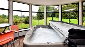 A spa room with a hot tub, large windows, and a view of a green landscape. - Luxury Estate with Pool & Spa (Jamoigne)