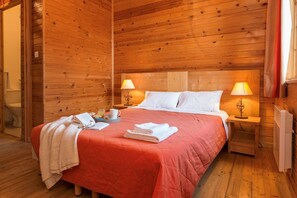Ein Zimmer mit Holzboden, einem Bett, zwei Nachttischlampen, einem Nachttisch und einem Fenster mit Vorhängen.