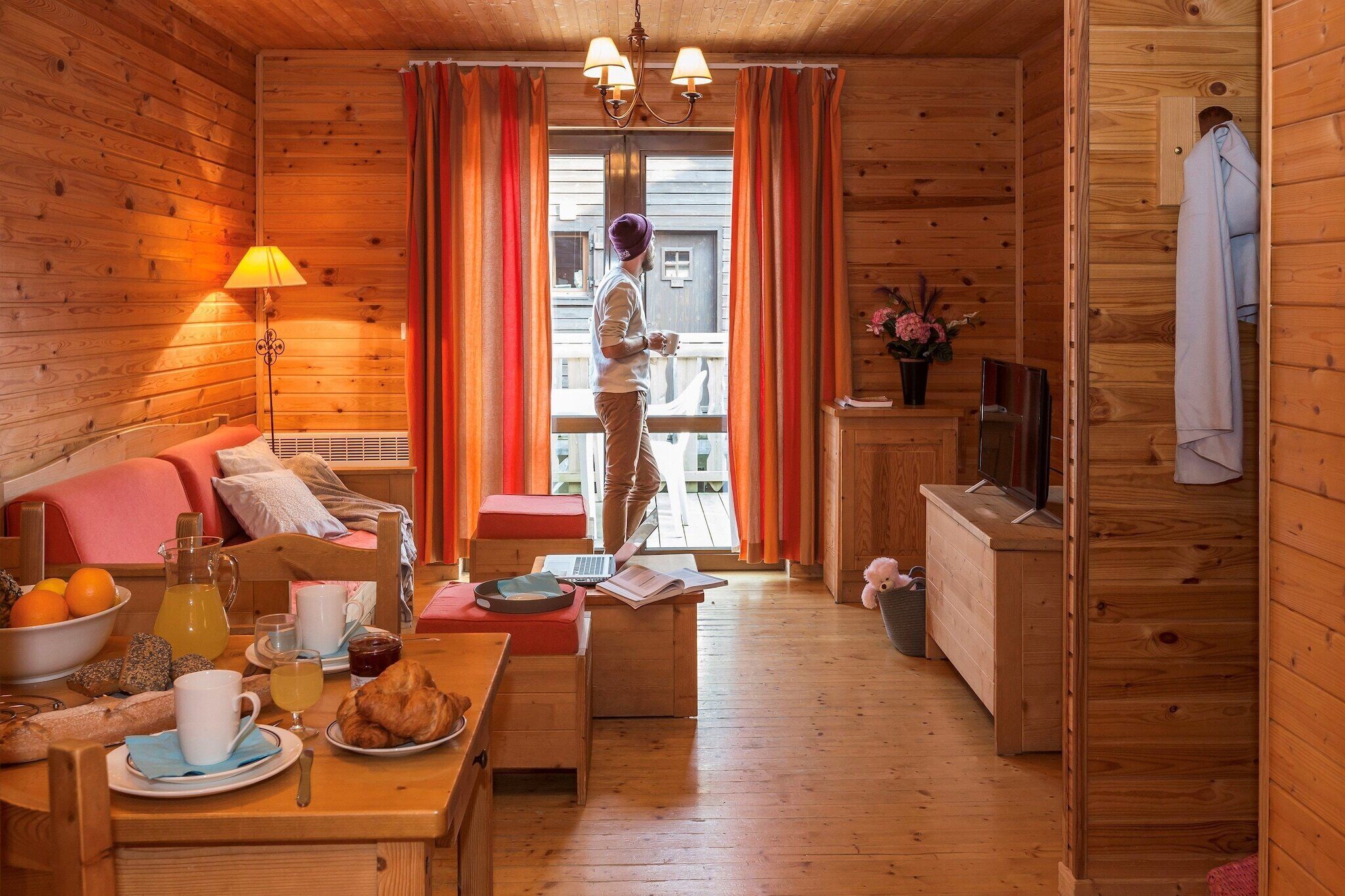 L’intérieur chaleureux d’un chalet avec un canapé, une table à manger et une personne debout près d’une fenêtre.