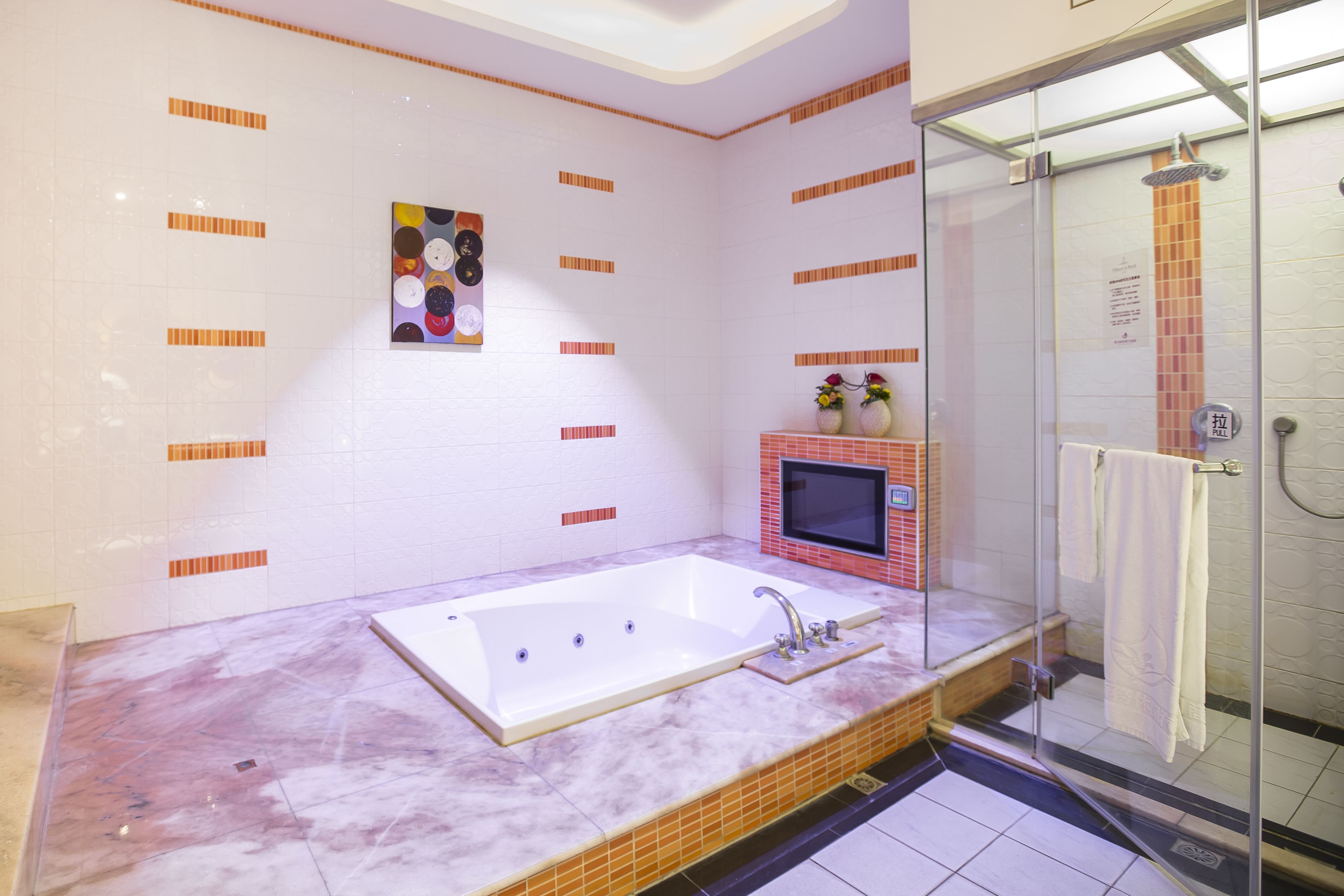 Ein modernes Badezimmer mit einer großen Badewanne, einer Duschkabine aus Glas und einem kleinen Fernseher an der Wand.