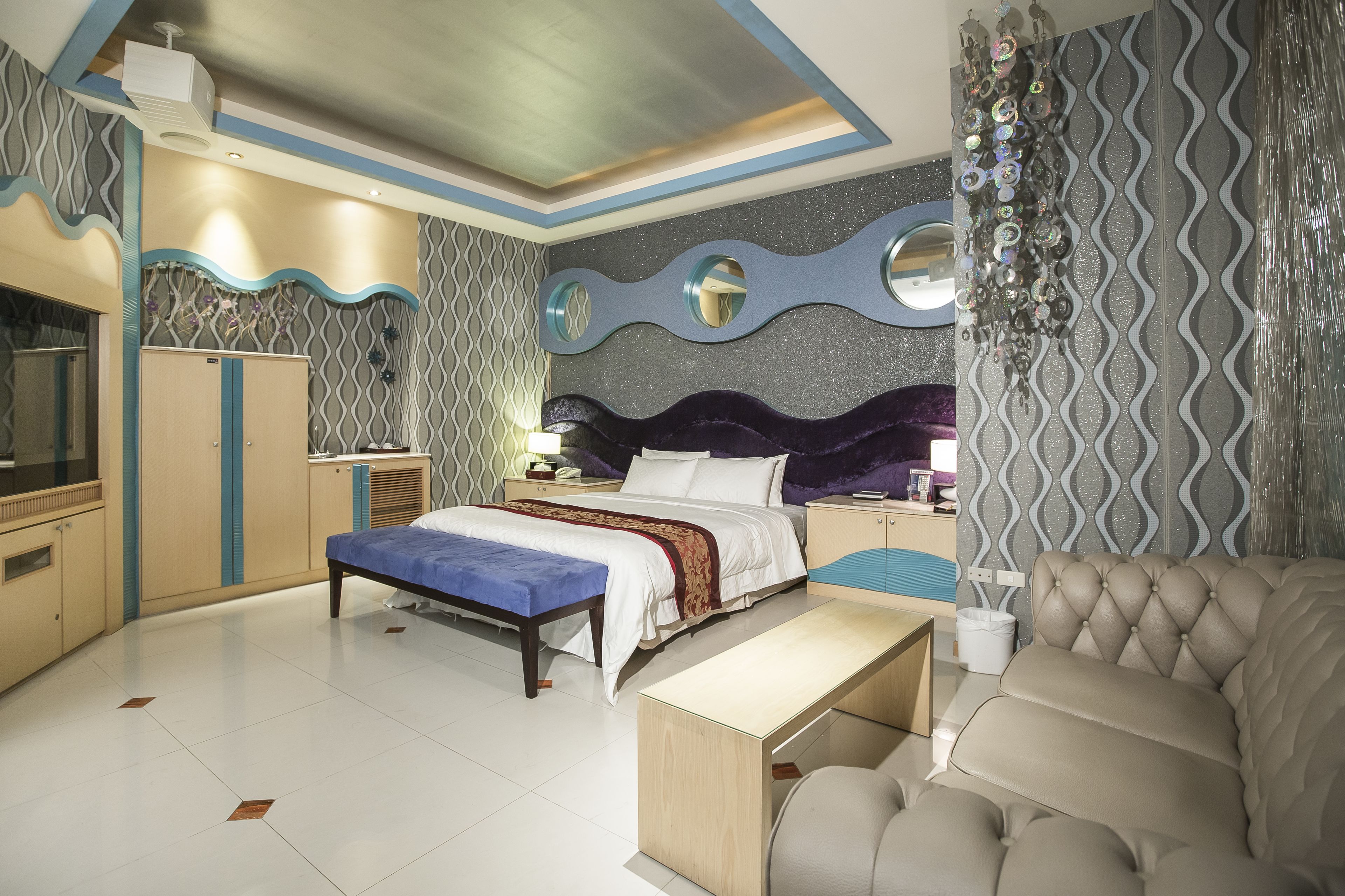 Quarto moderno com cama, mesas de cabeceira, um banco, um sofá e uma TV.