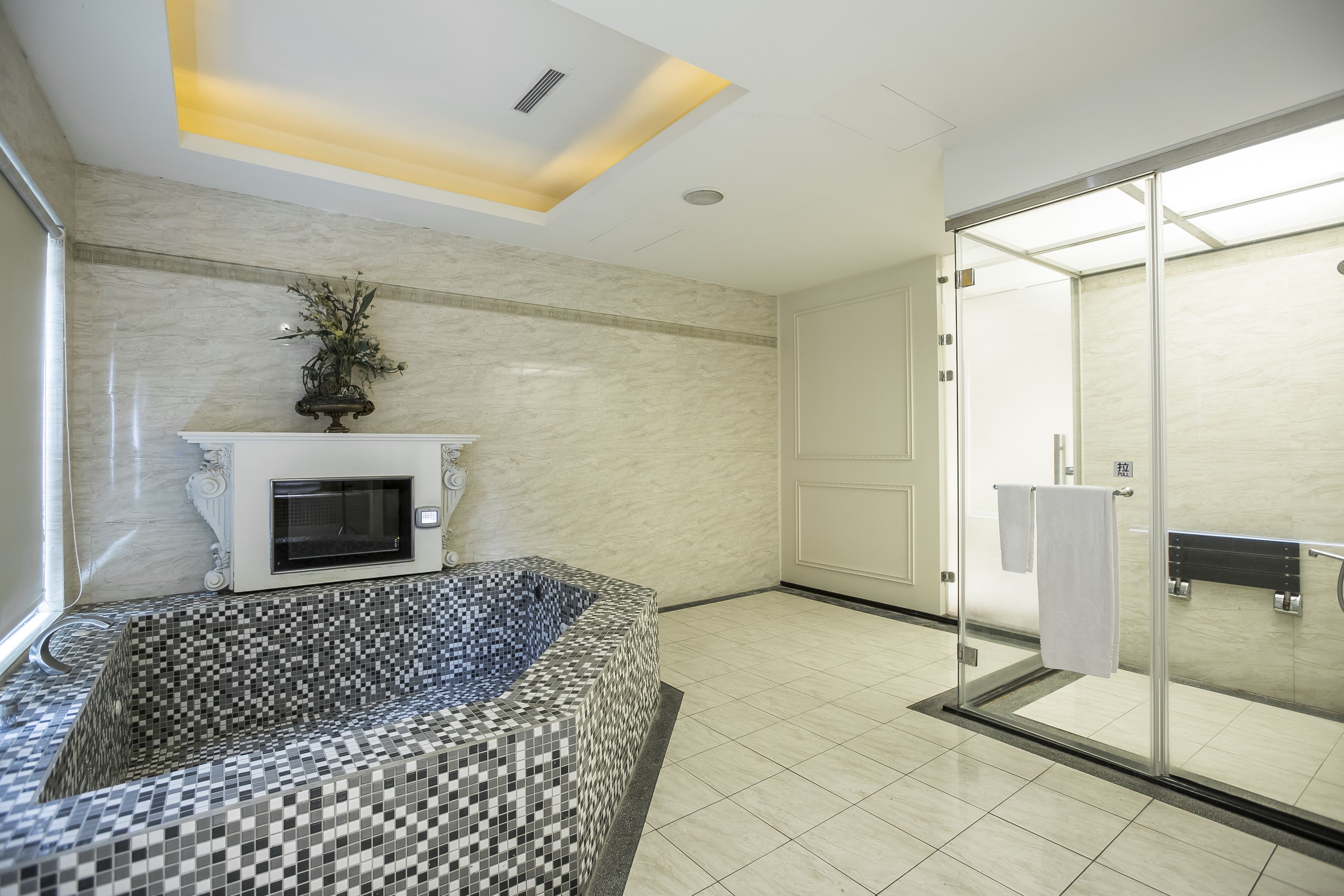 A modern bathroom with a mosaic bathtub, a glass shower enclosure, and a white fireplace.