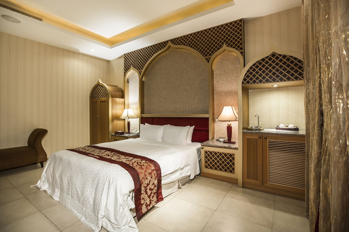 Een hotelkamer met een groot bed, een houten nachtkastje, een bureau en een stoel.
