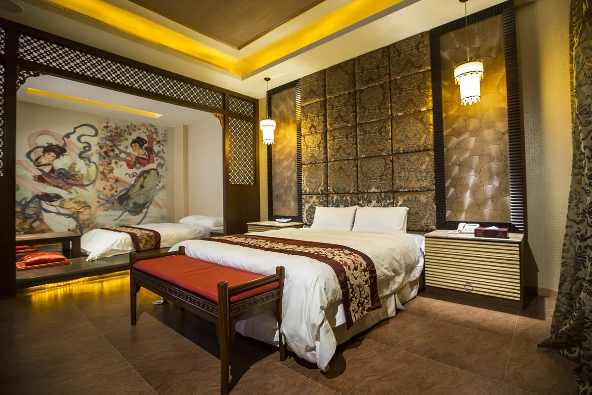 Een hotelkamer met een groot bed, twee kleinere bedden, een bureau en een decoratieve wand met kunstwerken.