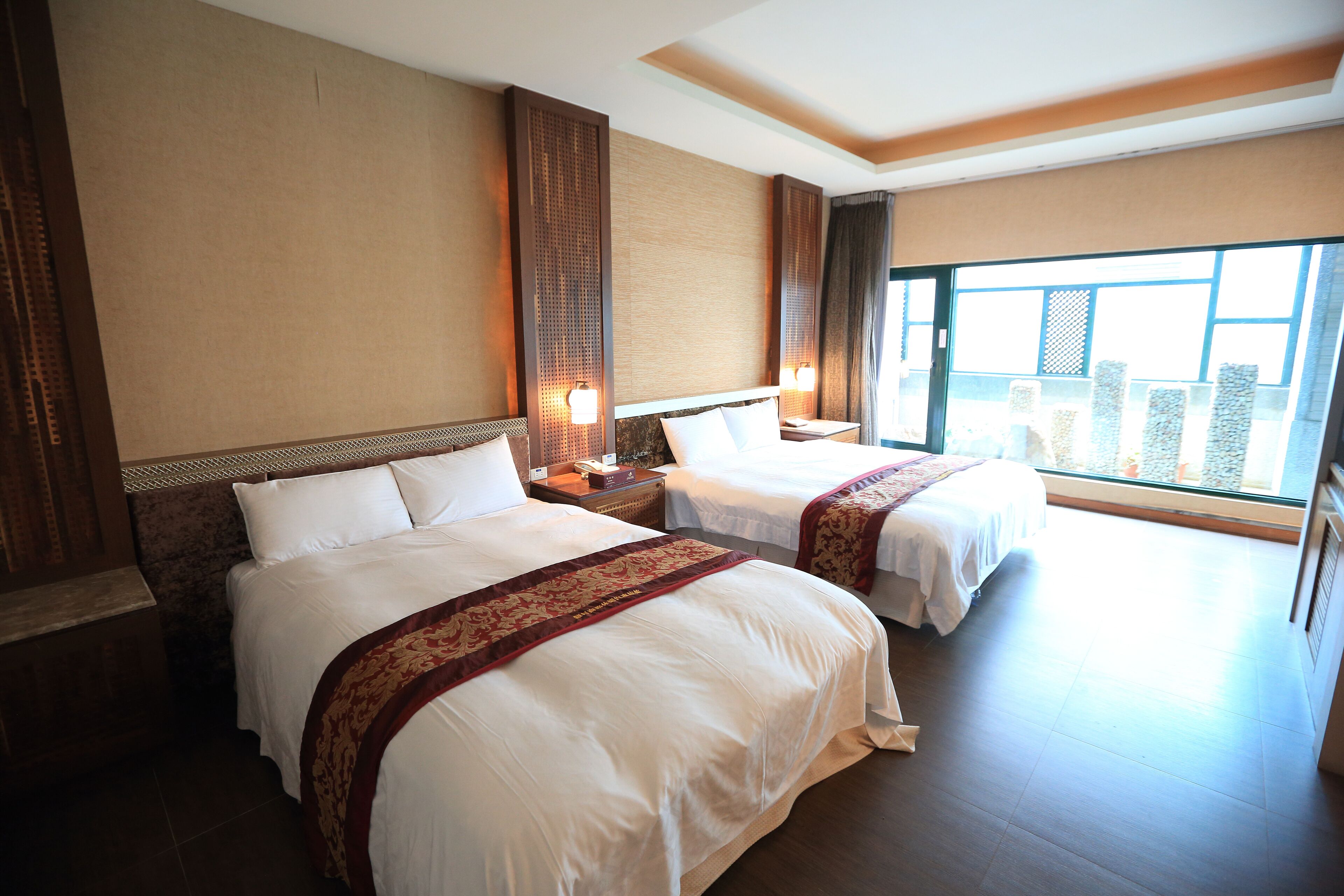 A hotel room with two beds, a large window, and a view of buildings.