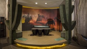 Een kamer met een centraal zite hoek, een structuur aan de muur die op een cactus lijkt, en een muurschildering van paarden.