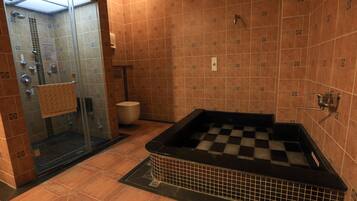 A bathroom with a checkered bathtub, a glass shower enclosure, and tiled walls.