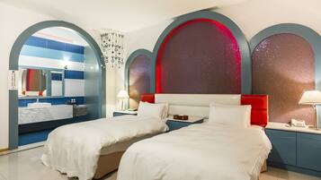 A hotel room with two beds, a bathroom with a mirror and sink, and a view of the night sky through arched windows.