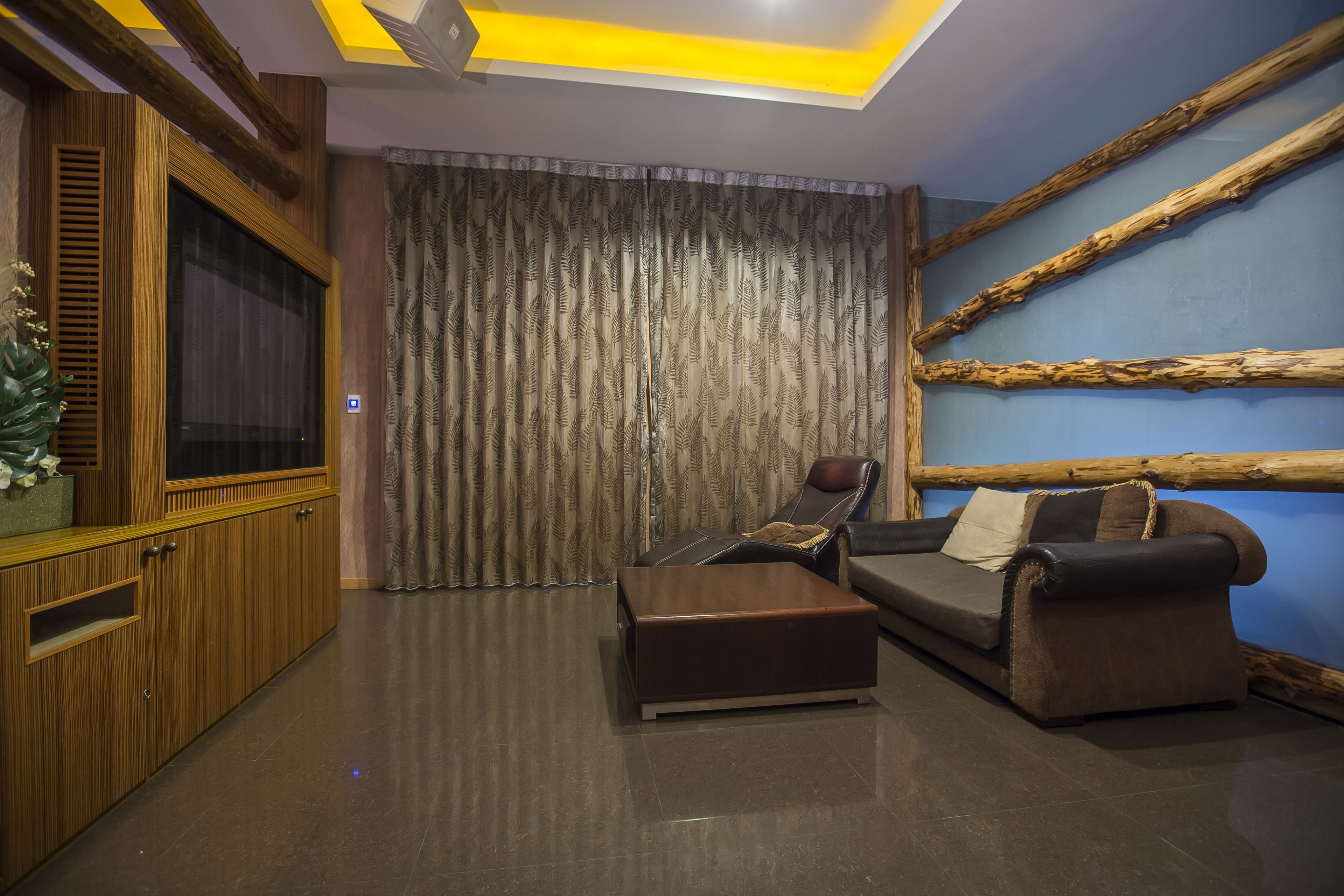 Un salon moderne avec un canapé, un pouf et un téléviseur posé sur un meuble en bois.