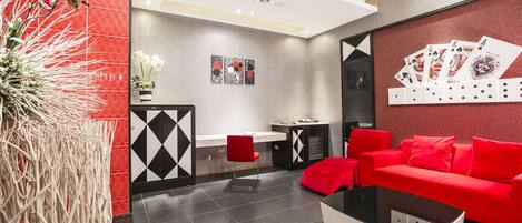 A modern living room with a red sofa, a glass coffee table, and a red chair. There is a small table with a vase of flowers and a painting on the wall.