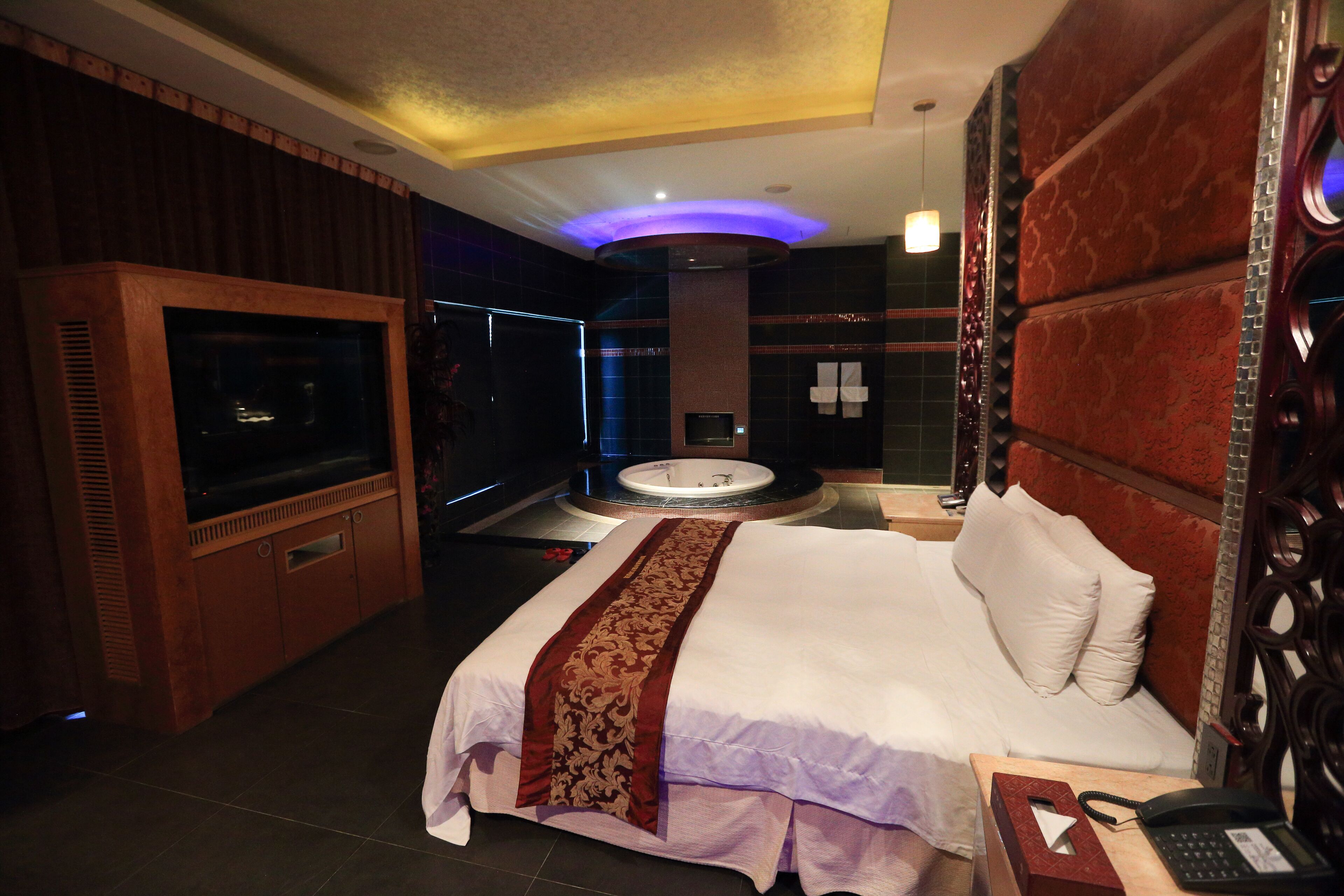 A hotel room with a large bed, a television, a bathtub, and a desk with a telephone.