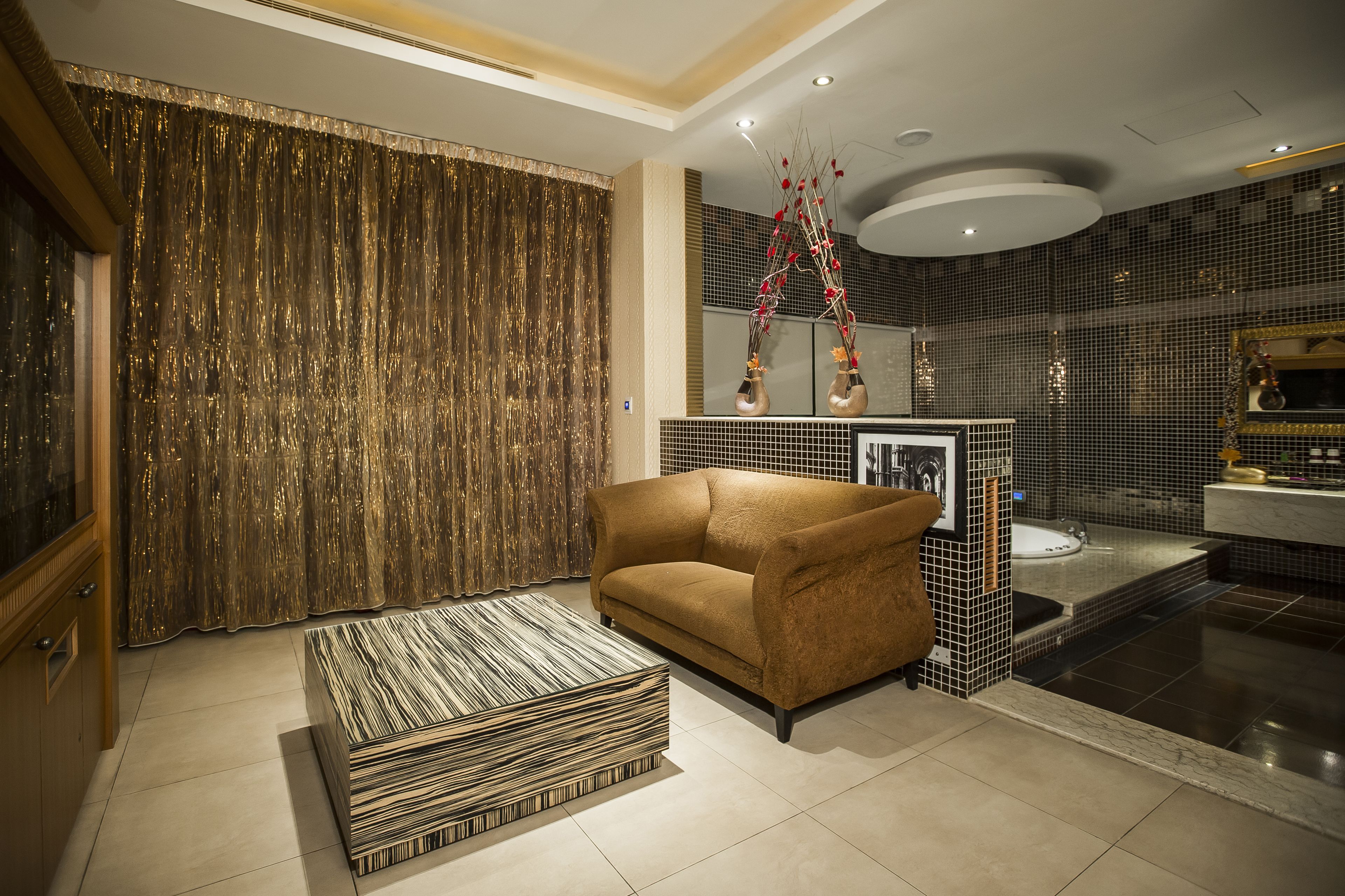 Una sala de estar moderna con un sofá, un taburete estampado, un jarrón decorativo y una pared de azulejos.