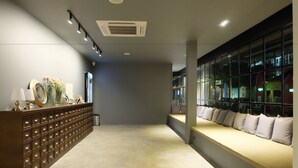 A hotel lobby with a long reception desk, a seating area with cushions, and large windows offering views of the outside. - Srianunt Boutique Hotel (Buriram)