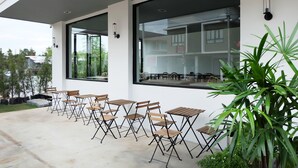A modern outdoor seating area with wooden tables and chairs, large windows, and potted plants. - Srianunt Boutique Hotel (Buriram)