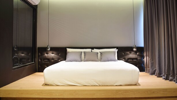 A modern bedroom with a large bed, dark headboard, and a built-in air conditioning unit. - Srianunt Boutique Hotel (Buriram)
