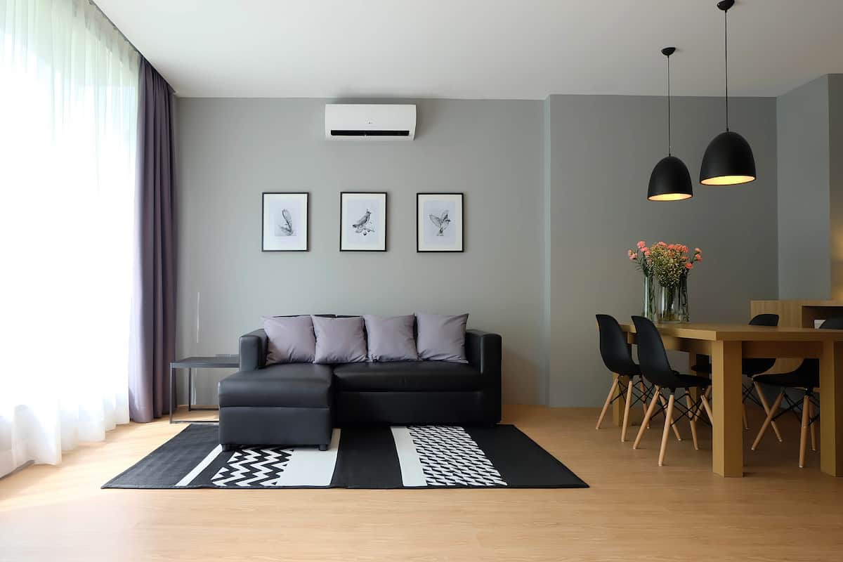 En moderne stue med en sort modulsofa, et spisebord med stole og et stort vindue med lette gardiner.