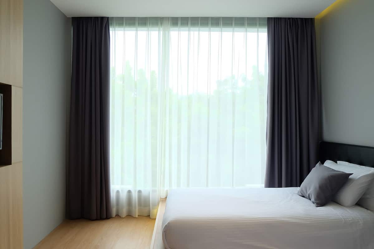 Et hotelværelse med en stor seng, mørke gardiner og udsigt til træer gennem vinduet.