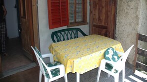 Un comedor con una mesa cubierta por un mantel amarillo con motivos florales, rodeada de sillas blancas con cojines verdes.