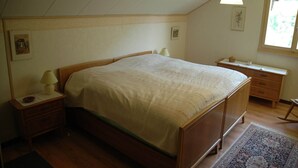 Un dormitorio con cama de madera, una mesita de noche con lámpara, cómoda y ventana con vistas.